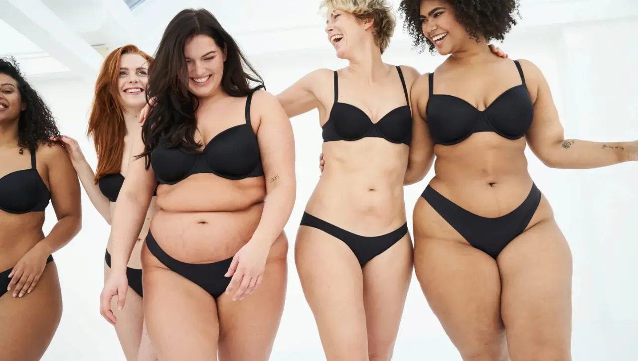 Vijf lachende vrouwen met uiteenlopende lichaamstypes en borsttypes in zwarte lingerie